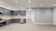 Located at 8940 Reseda Blvd in Northridge, California, this single-floor unit offers a thoughtfully designed modern interior with clean lines and a neutral color palette throughout. The open-concept kitchen is a standout feature, showcasing matte gray flat-front cabinetry, crisp white countertops, a tiled backsplash, and a full suite of stainless steel appliances including a gas range, built-in microwave, dishwasher, and side-by-side refrigerator. Large-format tile flooring flows throughout the main living and kitchen areas, lending a cohesive, contemporary feel. The living area is open and versatile, with recessed lighting illuminating the soft gray walls and clean white trim. Bedrooms feature ample natural light from large windows with vertical blinds, and one room includes a sliding mirror-door closet with built-in shelving. Sliding glass doors in one of the rooms open to a private balcony with views of mature trees. The two bathrooms are finished in a minimalist style, each featuring large-format tile flooring, white walls, and glass-enclosed tub-shower combinations. One bathroom includes a sleek gray vanity with a white countertop. Throughout the space, recessed lighting and modern fixtures reinforce the clean, move-in-ready aesthetic.