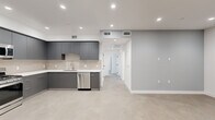 Located at 8940 Reseda Blvd in Northridge, California, this single-floor unit offers a thoughtfully designed modern interior with clean lines and a neutral color palette throughout. The open-concept kitchen is a standout feature, showcasing matte gray flat-front cabinetry, crisp white countertops, a tiled backsplash, and a full suite of stainless steel appliances including a gas range, built-in microwave, dishwasher, and side-by-side refrigerator. Large-format tile flooring flows throughout the main living and kitchen areas, lending a cohesive, contemporary feel. The living area is open and versatile, with recessed lighting illuminating the soft gray walls and clean white trim. Bedrooms feature ample natural light from large windows with vertical blinds, and one room includes a sliding mirror-door closet with built-in shelving. Sliding glass doors in one of the rooms open to a private balcony with views of mature trees. The two bathrooms are finished in a minimalist style, each featuring large-format tile flooring, white walls, and glass-enclosed tub-shower combinations. One bathroom includes a sleek gray vanity with a white countertop. Throughout the space, recessed lighting and modern fixtures reinforce the clean, move-in-ready aesthetic.