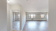 This 1-bedroom, 1-bathroom residence offers a clean, modern aesthetic throughout its efficiently designed single floor. The open-concept living and kitchen area serves as the heart of the home, featuring light hardwood-style flooring that flows seamlessly throughout. Large black-framed windows line the living space, inviting generous natural light and framing elevated city views. Baseboard heating and wall-mounted HVAC units ensure year-round comfort.

The kitchen is outfitted with sleek grey shaker cabinetry, white countertops, a subway tile backsplash, and a full suite of stainless steel appliances including a refrigerator, range, microwave, and dishwasher. A track lighting fixture overhead adds a contemporary touch.

The bedroom is a well-proportioned retreat with neutral grey walls, hardwood-style flooring, a window with exterior views, and a built-in closet providing convenient storage. The entrance connects the spaces with ease.

The bathroom is finished in a crisp, modern style with white wall tile, a soaking tub with overhead rain shower, a floating vanity with an integrated sink, and a mirrored medicine cabinet. Tile flooring and recessed lighting complete the polished look of this functional and stylish space.