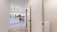 This single-floor residence showcases a contemporary design with a cohesive aesthetic carried throughout every room. Light wood-tone flooring runs continuously across the entire unit, creating a warm and unified feel. The open-concept kitchen serves as a central highlight, featuring a mix of white upper cabinetry and warm wood-toned lower cabinets set against a gray tile backsplash. A center island with a clean white finish provides additional workspace and casual seating. Stainless steel appliances, including a refrigerator, range, microwave, and dishwasher, complete the functional layout. Pendant lighting with a glass design hangs above the island, adding a decorative touch. Recessed lighting illuminates the space from above. The bedrooms offer clean, neutral walls with natural light provided by windows fitted with horizontal blinds. One bedroom includes access to a spacious walk-in closet outfitted with built-in shelving and hanging rods on multiple walls. The bathroom features a wood-toned vanity with a white countertop, an undermount sink with a matte black faucet, and a glass-enclosed shower with marble-style tile. A dedicated laundry area with shelving above rounds out this well-appointed home.