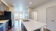 Located at 3705 Canfield St in Boulder, Colorado, this well-appointed one-bedroom, one-bathroom residence offers a thoughtfully designed single-level layout. The open-concept kitchen and living area serves as the heart of the home, showcasing rich dark hardwood flooring, recessed lighting, and a striking center island with a white countertop and integrated sink with a gold-toned faucet. Dark espresso cabinetry lines the kitchen walls, complemented by a full suite of stainless steel appliances including a refrigerator, electric range, and over-the-range microwave. The living area flows naturally from the kitchen, benefiting from natural light through forward-facing windows. The bedroom is a calm, carpeted retreat featuring a large double-door closet for ample storage and a window with outdoor views of the surrounding Boulder landscape. The bathroom is clean and functional, outfitted with a full soaking tub and shower combination featuring brushed nickel fixtures set against crisp white walls. A connecting hallway ties the spaces together efficiently. The overall ambiance is modern and comfortable, with a neutral palette and quality finishes throughout.