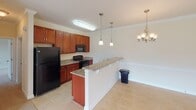 This single-story residence at Avalon Park in Mooresville, North Carolina offers a thoughtfully designed layout with warm, neutral tones throughout. The kitchen serves as a central highlight, featuring rich cherry wood cabinetry, granite countertops, and black appliances including a range, microwave, and refrigerator. A peninsula with pendant lighting above connects the kitchen to the adjacent dining area, which is accented by a chandelier and crown molding. Tile flooring extends through the kitchen and dining space, providing a durable, easy-to-maintain surface.

The living room is generously sized, finished with plush carpeting, crown molding, a ceiling fan, and direct access to an outdoor balcony through a glass door that brings in natural light. The bedrooms are carpeted and well-lit by large windows with exterior views. The primary bathroom includes a double-sink granite vanity with dual mirrors, a separate toilet compartment with grab bars, and a tub-shower combination. A dedicated laundry area includes washer and dryer hookups, a wire shelving rack, and electrical connections. Throughout the unit, consistent warm beige walls and tile or carpet flooring create a cohesive, comfortable atmosphere.