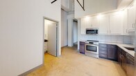 Located at 104 E Second St in Richmond, VA, this single-floor space showcases a distinctive industrial aesthetic throughout. The open layout is anchored by soaring ceilings that expose overhead ductwork and structural elements, lending the space a loft-like character with generous vertical volume.

The kitchen is a standout feature, outfitted with a two-tone cabinet design pairing crisp white upper cabinets with rich, dark lower cabinetry. Light stone countertops, a classic subway tile backsplash, and a full suite of stainless steel appliances — including an electric range, built-in microwave, and dishwasher — complete the functional and stylish cooking space.

The main living areas feature polished concrete flooring throughout, reinforcing the industrial character while providing a durable, low-maintenance surface. Tall white walls and an abundance of recessed lighting keep the interior bright and airy.

The bathroom is well-appointed with a white vanity topped by a dark granite countertop, a full soaking tub with tiled surround, brushed nickel fixtures, and grab bars for added convenience. Additional storage is provided by a walk-in closet accessible from the main living area. An electrical panel is conveniently integrated into the living space, and the overall layout offers a flexible, open floor plan suited to a variety of uses.