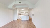 This single-story, 3-bedroom, 1-bathroom home offers a thoughtfully arranged layout across one floor. The entry immediately impresses with soaring vaulted ceilings and a large arched window that floods the living area with natural light, creating an airy and welcoming atmosphere. Wood-look flooring flows consistently throughout the main living spaces, lending warmth and visual continuity.

The open-concept design connects the living room seamlessly to the kitchen, which is a standout feature of the home. White cabinetry lines the walls, complemented by dark countertops and a central island with additional counter space — ideal for meal preparation or casual dining. White appliances, including a range and refrigerator, are included. A ceiling-mounted light fixture provides bright, even illumination over the kitchen workspace.

The three bedrooms are well-proportioned, each featuring wood-look flooring and clean white walls. The primary bedroom offers a comfortable footprint with dedicated closet access. A hallway connects the private areas of the home, which also includes a dedicated closet for additional storage.

The bathroom features a full tub-shower combination surrounded by classic white tile, a small window for natural light and ventilation, and a dark-countered vanity. The overall aesthetic throughout the home is clean, neutral, and move-in ready.