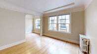 Located at 708 NW 19th Ave in Portland's vibrant Northwest District, this single-floor unit offers a thoughtfully arranged layout that makes efficient use of its cozy footprint. The living area greets you with warm hardwood floors, a textured ceiling with classic crown molding, and multiple large windows that flood the space with natural light and offer views of the surrounding urban streetscape. A graceful arched doorway connects the main living area to an adjoining room, adding architectural character and a sense of depth. The combined dining and kitchen area is well-appointed with white cabinetry extending to the ceiling for ample storage, tile backsplash, dark countertops, and a full suite of white appliances including a range and refrigerator. Hexagonal tile flooring anchors the kitchen space. A hallway leads to the bathroom, which features a classic pedestal sink, a built-in medicine cabinet, and a tub/shower combination set beneath an arched enclosure with a window for natural ventilation. The hallway also includes a wall-mounted vanity with mirror and a built-in multi-drawer closet with brushed hardware, providing smart, integrated storage. Throughout, the warm neutral palette and preserved vintage details give the space a timeless, livable character.