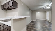 This single-floor unit offers a clean, modern aesthetic defined by rich, dark hardwood-style flooring that flows seamlessly throughout every room. The open living area is generously proportioned, featuring a ceiling fan with light fixture, a textured ceiling, and a large window that invites natural light. It connects effortlessly to the kitchen via a breakfast bar with a speckled quartz-look countertop, making the space ideal for both everyday living and entertaining.

The galley-style kitchen is efficiently designed with dark espresso cabinetry lining both walls, complemented by light quartz-look countertops, a mosaic tile backsplash, and white appliances including a range and refrigerator. A stainless steel sink and built-in range hood complete the functional layout.

The bedrooms continue the consistent flooring and neutral warm-gray wall palette, each equipped with ceiling fans and windows fitted with blinds that allow for natural light control. The rooms offer a comfortable sense of space with clean, simple finishes.

The bathroom features large-format marble-look wall tiles surrounding a soaking tub and shower combination, paired with a built-in corner shelf for added convenience. The textured ceilings and neutral tones throughout the unit create a cohesive and inviting atmosphere.