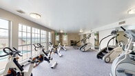 Located at 2100 Rebsamen Park Rd in Little Rock, Arkansas, this fitness center offers a well-appointed single-room workout facility designed to support a comprehensive exercise routine. The space is finished with durable, low-pile carpeting in a neutral gray tone, and the walls are painted in a warm greige, creating a clean and functional atmosphere throughout.

The room is generously stocked with a wide variety of cardio equipment, including multiple stationary spin bikes by TRUE Fitness, StairMaster steppers, elliptical cross-trainers, and treadmills — providing ample options for cardiovascular training. A dedicated strength and free-weight area features a multi-tiered dumbbell rack alongside an adjustable weight bench, accommodating a range of resistance workouts.

A full-length mirrored wall spans one side of the room, visually expanding the space and allowing users to monitor their form during exercise. Flush-mounted ceiling lights provide bright, even illumination throughout. Large windows along one wall invite natural light and offer views of the surrounding greenery, enhancing the overall workout environment. Multiple entry doors provide convenient access points to the facility. This fitness center delivers a practical and well-rounded space for residents seeking a dedicated on-site exercise amenity.