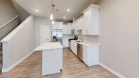 Located in Byron, Minnesota, this well-appointed two-story home offers 3 bedrooms and 3 bathrooms across two thoughtfully designed floors. The main level features an open-concept layout connecting the living room and kitchen, creating an inviting, airy atmosphere. A standout stone-surround fireplace with a classic white mantel anchors the living area, adding warmth and character. The kitchen is equipped with white shaker cabinetry, quartz countertops, stainless steel appliances, a central island with seating, and pendant lighting — a highly functional and attractive space for cooking and entertaining. A convenient half bathroom is also located on the main floor. Light-toned luxury vinyl plank flooring runs throughout both levels, lending a clean, cohesive look. The upper floor houses all three bedrooms, including a spacious primary suite with a walk-in closet featuring wire shelving and a private en-suite bathroom with a dual-sink vanity and tub/shower combo. Additional bedrooms include closets with built-in shelving. A dedicated laundry room with full-size washer and dryer hookups and overhead shelving adds everyday practicality. Neutral gray-toned walls and recessed lighting throughout contribute to the home's bright, modern aesthetic.