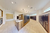 Located at 1700 Katy Fort Bend Road in Katy, Texas, this mail room serves as a well-appointed, functional communal space designed with both practicality and aesthetic appeal in mind. The room is finished with light-toned tile flooring throughout, complementing the clean white walls and creating a bright, welcoming atmosphere.

A standout feature of the space is the central freestanding island constructed from warm-toned wood, which houses multiple rows of individual dark metal mailboxes. This central unit also incorporates a white countertop surface, providing a convenient area for sorting mail. Additional banks of dark metal mailboxes are mounted along the surrounding walls, framed in matching wood trim, ensuring ample mailbox capacity for a large number of residents.

Overhead, a cluster of geometric hexagonal pendant lights serves as a striking design element, providing modern, stylish illumination throughout the room. Recessed ceiling lights supplement the overall brightness of the space. A glass-paneled door on one side of the room allows natural light to filter in and provides easy access. Decorative framed wall art adds a refined touch to the otherwise utilitarian setting. Clearly posted signage identifies the space as the mail room for 1700 Katy Fort Bend Road, reinforcing its dedicated purpose within the building.