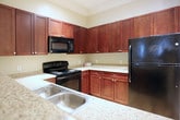 This single-floor residence offers a thoughtfully designed layout with a cohesive neutral color palette and warm finishes throughout. The kitchen is equipped with rich dark-red cabinetry, granite-style countertops, black appliances including a range, microwave, refrigerator, and dishwasher, complemented by hardwood-style flooring and track lighting with crown molding accents.

The dining area features crown molding, track lighting, and neutral carpet, providing a defined space for entertaining. The living room offers a ceiling fan, crown molding, natural light from a large window, and plush carpeting.

Multiple bedrooms are present, each with ceiling fans and carpet. One bedroom features a bold teal accent wall for a striking focal point, while others maintain soft neutral tones. The bathrooms include dark wood vanities with light countertops, tile flooring, and walk-in closets with wire shelving systems. One bathroom features an elongated vanity and shower with direct bedroom access.

A dedicated in-unit laundry area houses a full-size washer and dryer with overhead wire shelving. Crown molding, track lighting, and consistent warm tones contribute to an inviting, well-finished ambiance throughout the home.