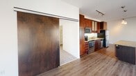 Located on West Lake Street in Minneapolis, this single-floor unit offers a thoughtfully designed layout with a clean, contemporary aesthetic. The open living area is a standout feature, with large floor-to-ceiling windows that flood the space with natural light and provide views of the surrounding urban neighborhood. Track lighting overhead adds a modern, flexible illumination option, while wood-finish flooring anchors the space with warmth.

The kitchen is well-appointed with rich dark wood cabinetry extending to the ceiling for ample storage, granite-style countertops, and a full suite of stainless steel appliances including a refrigerator, range, microwave, and dishwasher. A striking full-panel sliding barn door separates the kitchen area from the carpeted bedroom, offering both a design focal point and practical flexibility.

The bedroom benefits from its own large window with a roller shade, plush carpet, and a ceiling fan with light fixture. A closet with sliding white panel doors provides generous storage. The bathroom features a dual-sink vanity with a white countertop, dark wood cabinetry, a wood-framed mirror, and classic subway tile detailing in the shower area. Throughout, the unit maintains a cohesive modern palette of white walls and warm wood tones.