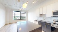 Located at 2528 Texas Ave in St. Louis's vibrant 63104 neighborhood, this single-floor loft-style residence blends industrial character with modern design. Light hardwood flooring flows continuously throughout the open layout, grounding each space with warmth and cohesion.

The kitchen and living area form a bright, open-concept hub anchored by a large waterfall-edge island with a sleek stone countertop. Cabinetry in crisp white and matte charcoal pairs with gold-tone hardware and faucet fixtures, while a white hexagonal tile backsplash adds geometric texture. An artistic pendant light in an organic form hangs overhead, complementing the exposed ceiling detail that nods to the building's industrial heritage. Oversized black-framed windows flood the space with natural light and frame open views of the surrounding St. Louis cityscape.

The bedroom areas are generously proportioned and bathed in natural light, with the same expansive black-framed windows delivering elevated outdoor views. Dark espresso-toned sliding closet doors with brass hardware add a bold, sophisticated contrast to the crisp white walls.

The bathroom is appointed with full subway tile surrounding the soaking tub and shower, matte black fixtures, a floating warm wood vanity with an integrated white sink, and a sleek black-framed illuminated mirror — creating a clean, spa-like aesthetic throughout.