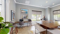 Located at 200 S Mallory St in Hampton, Virginia, this single-floor office space offers a thoughtfully designed environment that balances collaborative and individual work needs. The open layout is anchored by a large central conference-style table with upholstered bar-height seating, making it ideal for group meetings or shared work sessions. A wall-mounted flat-screen television and wall sconces lend a polished, professional atmosphere, while crown molding and soft blue-gray walls add architectural character and a calming aesthetic.

Rich wood cabinetry with granite countertops lines one wall, providing functional storage and surface space alongside a printer station. Light wood-look tile flooring runs throughout, complemented by a vibrant, multi-toned area rug that adds warmth and visual interest. Individual workstations equipped with desktop computers and bar-height seating are positioned near large windows fitted with roller shades, offering views of the surrounding greenery while allowing for natural light control.

Comfortable lounge seating is tucked into windowed nooks, creating inviting spots for focused work or casual conversation. Local artwork adorns the walls, giving the space a distinct sense of place. French doors open to additional areas, enhancing the sense of openness and connectivity throughout this well-curated, modern office environment.