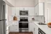 This 740-square-foot, single-story unit at 13601 S 44th St in Phoenix, AZ offers a practical and modern layout across two bedrooms and one bathroom. Wood-look flooring runs consistently throughout the entire unit, contributing to a cohesive and clean aesthetic.

The open-concept kitchen and living area serves as the heart of the unit. The kitchen features white shaker cabinetry, white quartz countertops, a peninsula with an integrated sink, subway tile backsplash, and stainless steel appliances including a refrigerator, range, and microwave. The living area benefits from a ceiling fan, sliding glass door access to an outdoor patio, and multiple windows that bring in natural light and exterior views of surrounding greenery.

The primary bedroom measures 150 square feet and includes a ceiling fan, multiple windows with outdoor views, a sliding glass door to the patio, and access to a spacious walk-in closet with dual hanging rods and built-in shelving. The bathroom features a white vanity with brushed nickel hardware and wood-look flooring. A dedicated laundry room houses a full-size washer and dryer. Crown molding and neutral-toned walls are consistent details throughout the unit.