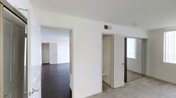 This single-floor residence presents a clean and functional layout with a neutral color palette throughout. The interior is characterized by crisp white walls and ceilings that lend a bright, open feel to the space. A seamless flow connects the rooms, offering an accessible and practical floor plan.

The flooring transitions between rich dark hardwood-style planks in the main living areas and soft carpet in the bedroom zones, providing both visual contrast and comfort underfoot. Built-in shelving is incorporated into the closet space, offering organized storage solutions with multiple tiers ideal for keeping belongings neatly arranged.

A mirrored closet door in the bedroom area reflects natural light from a nearby window, enhancing the sense of openness. Overhead HVAC vents are integrated into the ceilings, ensuring efficient climate control throughout. Interior doors feature classic paneled designs with white finishes that complement the overall aesthetic.

The space is well-lit with natural light filtering in through windows, contributing to a welcoming ambiance. The minimalist, move-in-ready condition of the interior allows residents to personalize and furnish to their own taste. Overall, this space offers a practical, comfortable, and versatile living environment with thoughtful storage and a cohesive design throughout.