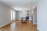 Located at 1701–1731 American Royal Dr in Kansas City, MO, this single-floor unit features a clean, modern design with a neutral color palette throughout. The open-concept living and kitchen area serves as the heart of the space, anchored by warm-toned hardwood flooring that extends across the main living zones. Sliding glass doors and multiple windows allow natural light to pour into the living area, offering outdoor views and a bright, airy atmosphere.

The kitchen is well-appointed with white high-gloss cabinetry, a classic grid-pattern tile backsplash, stainless steel appliances including a range and refrigerator, and a stainless wall-mounted range hood. A rustic wood-topped island provides additional prep and dining space, complemented by sleek pendant lighting overhead. Recessed lighting throughout the open area adds to the contemporary feel.

The bedroom features plush carpeting, tall windows with outdoor views, and access to a generously sized walk-in closet equipped with wire shelving systems. Two bathrooms serve the unit — one with a tub/shower combination behind sliding glass doors, and another with a standalone glass-door shower enclosure. In-unit laundry connections are also present, adding everyday convenience to this well-designed space.
