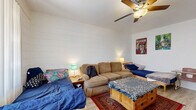 Located at 1130 E Orange St in Tempe, Arizona, this single-story, one-bedroom, one-bathroom unit offers a practical and functional layout well-suited for everyday living. The interior is characterized by painted cinder block walls that lend a sturdy, utilitarian aesthetic throughout the space, complemented by light wood-style flooring and ceiling fans in key areas to support comfort in the Arizona climate.

The open-concept main area seamlessly combines the living room, dining space, and kitchen into one cohesive zone. The living area benefits from a sliding glass door that introduces natural light and provides access to an exterior balcony or patio. This multifunctional room offers generous flexibility for arranging furnishings.

The bedroom is notably spacious for a unit of this size, accommodating a full sleeping and workspace setup with room to spare. A large window fills the room with natural light, and a ceiling fan adds to the comfort. Two closets with louvered bi-fold doors provide ample storage, along with a utility panel conveniently located in the room.

The bathroom features a clean white vanity with under-sink storage, a wall mirror with overhead lighting, and a tub-shower combination enclosed by a curtain with classic tiled walls. A connecting hallway ties the rooms together, completing this efficiently designed single-floor layout.