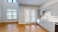 This thoughtfully designed two-story home offers a compelling blend of modern finishes and functional layout across two well-proportioned floors. The main level makes an immediate impression with its soaring ceilings and polished stained concrete floors in a warm amber tone, lending the open living and kitchen area an industrial-chic character. The kitchen is well-appointed with gray shaker-style cabinetry, white subway tile backsplash, stainless steel appliances including a range, built-in microwave, refrigerator, and dishwasher, all complemented by clean white countertops. French doors on the main level invite abundant natural light and provide outdoor access, while additional windows further brighten the living space. A convenient half bathroom on the main floor features matching gray cabinetry and the same stained concrete flooring. Upstairs, rich dark hardwood-style flooring carries through the bedroom level. The primary bedroom is generously sized, featuring its own set of French doors with a ceiling fan overhead. A walk-in closet with wire shelving provides ample storage. Two full bathrooms serve the upper level, one featuring classic white penny tile flooring, white subway tile surround, a tub-shower combination, and a gray vanity — consistent with the home's cohesive modern aesthetic throughout.