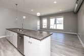 Located at 550 Watson Powell Jr Way in the heart of downtown Des Moines, this two-bedroom, two-bathroom residence offers a well-designed single-floor layout with a clean, contemporary aesthetic throughout. The open-concept kitchen and living area serves as the centerpiece of the home, showcasing a striking large-format granite island with an undermount sink and pendant lighting overhead. Dark espresso cabinetry contrasts elegantly with a white subway tile backsplash, while stainless steel appliances complete the modern kitchen. Light wood-look flooring runs throughout the main living and kitchen areas, enhancing the bright, airy feel. The living room features multiple large windows and a glass-paned door that floods the space with natural light and offers views of the surrounding urban landscape. Both bedrooms are carpeted and generously proportioned, with exposed industrial-style ductwork lending an urban loft character. Each bathroom is finished with tub-shower combinations and stone-topped vanities. A long, well-lit corridor connects the rooms, featuring sleek panel doors and continued exposed ductwork along the ceiling, reinforcing the modern industrial design. This residence combines upscale finishes with a functional layout in a prime downtown location.