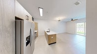 This modern single-story home features a thoughtfully designed open-concept layout that seamlessly connects the kitchen and dining area to the main living space. The kitchen is a standout, showcasing warm natural wood cabinetry with sleek black hardware, white quartz countertops, a central island with an undermount sink and matte black faucet, and stainless steel appliances including a French door refrigerator and electric range with overhead microwave. Large-format light tile flooring flows throughout, complementing the clean white walls and creating a bright, airy atmosphere. Skylights and ceiling fans add to the home's well-lit, comfortable ambiance, while a sliding glass door in the living area opens to a lush green outdoor space. The three bedrooms are well-proportioned, each featuring tile flooring, ceiling fans, and windows that invite natural light. The primary bedroom includes a dedicated walk-in closet with built-in shelving and hanging rods for ample storage. The bathrooms are elegantly finished, with one featuring a walk-in glass-enclosed shower, geometric patterned tile flooring, a wood vanity with white countertop, and matte black fixtures throughout. This home delivers a clean, contemporary aesthetic with quality finishes at every turn.