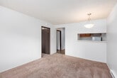 This single-floor residential unit offers a practical and comfortable layout designed for everyday living. The main living area is finished with wall-to-wall carpet in a warm neutral tone, creating a cozy atmosphere throughout. A textured ceiling and a pendant light fixture add character to the space, while baseboard heating units along the walls ensure efficient climate control. A window with blinds allows natural light to filter into the room, providing pleasant views of the surrounding greenery outside.

The layout, as revealed by the dollhouse view, includes a central hallway connecting the primary living spaces. A pass-through opening links the living area to the kitchen, enhancing the open feel between rooms. The kitchen area features dark cabinetry, adding a contrasting element to the otherwise light-toned interior.

The bedrooms continue the carpeted flooring and feature windows with blinds that bring in ample natural light. Baseboard heaters are present in each room, and the textured ceilings carry throughout, maintaining a consistent aesthetic across the unit.

The bathroom is clean and well-appointed, featuring a wood-toned vanity with an integrated sink, a framed mirror, and overhead lighting. A full shower-tub combination with a tiled surround and vinyl plank-style flooring rounds out this functional space. Overall, the unit presents a straightforward, well-maintained interior well-suited for comfortable daily living.