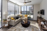 Located at 151 E Blount Ave in Knoxville, Tennessee, this well-appointed single-floor residence offers a thoughtfully designed layout with modern finishes throughout. The open-concept kitchen is a standout feature, equipped with crisp white shaker cabinetry, a subway tile backsplash, stainless steel appliances including a French door refrigerator, electric range, and built-in microwave, all centered around a spacious island with pendant lighting and bar seating — ideal for both everyday living and entertaining. In-unit stacked washer and dryer units are conveniently located just off the kitchen area. The living room is bathed in natural light, thanks to expansive floor-to-ceiling windows that frame views of the surrounding Knoxville streetscape. A ceiling fan and direct access door add functionality to this bright, open space. Wood-look flooring runs throughout the main living areas, while plush carpet adds comfort to the bedrooms. The primary bedroom features large windows with outdoor views and a ceiling-fan fixture. The bathroom is finished with white subway tile in the walk-in shower, a white vanity with ample storage, and wood-look flooring. Hallways are accented with decorative wall art, adding a modern aesthetic touch throughout the home.