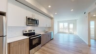 Located at 22330 Main St in Hayward, California, this thoughtfully designed single-floor residence showcases a clean, contemporary aesthetic throughout. The open-concept layout seamlessly connects the kitchen and living area, creating a bright and functional living environment.

The kitchen is a standout feature, outfitted with a full suite of stainless steel appliances including a refrigerator, electric range, over-the-range microwave, and dishwasher. Two-tone cabinetry pairs crisp white upper cabinets with warm wood-finish lower cabinets, complemented by a classic white subway tile backsplash and light quartz countertops. Light wood-tone luxury vinyl plank flooring flows throughout the main living areas, adding warmth and continuity.

The living area is generously proportioned and bathed in natural light, with a glass door providing direct access to a private balcony offering outdoor views of the surrounding neighborhood. An additional room off the main living space offers flexibility for various uses and also features balcony access.

The bedroom is carpeted for comfort and features a large window that frames pleasant exterior views and fills the room with natural light. The full bathroom is finished with large-format tile flooring, a wide wood-toned vanity with a full-width mirror, and a combined tub and shower enclosure, rounding out this well-appointed residence.