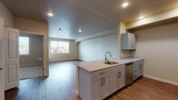 Located at 3805 SW Murray Blvd in Beaverton, Oregon, this single-floor unit offers a clean, modern design with a thoughtfully laid-out open floor plan. The kitchen is a standout feature, equipped with gray shaker-style cabinetry accented by brushed gold hardware, granite countertops, and a full suite of stainless steel appliances including a refrigerator, electric range, built-in microwave, and dishwasher. A peninsula with an undermount sink and additional counter space extends into the main living area, creating a seamless transition between cooking and entertaining spaces. The living area is generously sized, featuring warm wood-look flooring, recessed lighting, and a neutral color palette that lends a bright, welcoming ambiance. A large window brings in natural light and offers views of the surrounding neighborhood. The bedroom is carpeted for comfort and also benefits from a bright window. The bathroom is clean and functional, featuring a full tub and shower combination with tiled surround and wood-look flooring. Practical conveniences include an in-unit stacked washer and dryer. The overall design emphasizes modern finishes, efficient use of space, and a cohesive, contemporary aesthetic throughout.