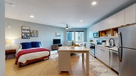 Located at 455 Snelling Ave N in Saint Paul, Minnesota, this modern studio offers a thoughtfully designed open-concept layout that efficiently combines living, sleeping, and dining functions into a single, cohesive space. Light blue and gray walls, recessed lighting, and light-toned hardwood-style flooring create a bright, contemporary ambiance throughout.

The kitchen is well-appointed with stainless steel appliances — including a refrigerator, electric range, microwave, and dishwasher — complemented by white cabinetry with open shelving accents and a hexagonal tile backsplash. A freestanding island provides additional prep and storage space, doubling as a dining area. The living area flows naturally from the kitchen, bathed in natural light from large windows that offer views of the surrounding neighborhood. A ceiling fan overhead adds comfort to the space.

The bathroom features a clean, modern design with a white vanity, an illuminated mirror, and a tub-shower combination. Consistent hardwood-style flooring carries through from the main living area, tying the space together seamlessly. This well-designed studio is ideally situated in the vibrant Snelling Avenue corridor, close to shops, dining, and public transit in Saint Paul.