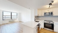 Located on the 26th floor at 100 Christopher Columbus Drive in Jersey City, NJ, this 2-bedroom, 2-bathroom residence offers a clean, modern aesthetic throughout. Light wood flooring flows continuously across the open-plan living and kitchen area, creating a warm and cohesive feel. The kitchen is outfitted with white shaker cabinetry, a subway tile backsplash, quartz countertops, a large center island, and a full suite of stainless steel appliances including a gas range, built-in microwave, dishwasher, and French door refrigerator. Track lighting adds a contemporary touch overhead. Both bedrooms are bright and airy, each featuring large picture windows that frame sweeping panoramic views of the Jersey City skyline and surrounding urban landscape, with abundant natural light streaming in throughout the day. The two bathrooms are finished with crisp white tile, hexagonal mosaic flooring, white vanities, and matte black fixtures — one includes a soaking tub with a curved shower rod, while the other features a glass-enclosed walk-in shower. Two closets and a hallway provide practical storage throughout. A stacked washer and dryer unit is also included within the residence.