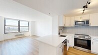 Located on the 26th floor at 100 Christopher Columbus Drive in Jersey City, NJ, this 2-bedroom, 2-bathroom residence offers a clean, modern aesthetic throughout. Light wood flooring flows continuously across the open-plan living and kitchen area, creating a warm and cohesive feel. The kitchen is outfitted with white shaker cabinetry, a subway tile backsplash, quartz countertops, a large center island, and a full suite of stainless steel appliances including a gas range, built-in microwave, dishwasher, and French door refrigerator. Track lighting adds a contemporary touch overhead. Both bedrooms are bright and airy, each featuring large picture windows that frame sweeping panoramic views of the Jersey City skyline and surrounding urban landscape, with abundant natural light streaming in throughout the day. The two bathrooms are finished with crisp white tile, hexagonal mosaic flooring, white vanities, and matte black fixtures — one includes a soaking tub with a curved shower rod, while the other features a glass-enclosed walk-in shower. Two closets and a hallway provide practical storage throughout. A stacked washer and dryer unit is also included within the residence.