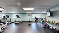 Located at 500 East Bruceton Road in Pittsburgh's Allegheny County, this 990-square-foot fitness facility spans a single floor and is thoughtfully organized into three distinct areas designed to support a comprehensive workout experience.

The main gym floor is the centerpiece of the space, finished with durable rubber flooring and illuminated by a drop-panel ceiling with recessed fluorescent lighting. The walls are painted in a calming teal-blue tone and lined with mirrors to maximize the sense of space. Equipment includes Matrix treadmills, elliptical trainers, a multi-station cable machine, rowing machines, recumbent and upright bikes, a stair stepper, and a rack of color-coded kettlebells. A wall-mounted flat-screen TV adds entertainment during workouts. Windows along the perimeter allow natural light to enter and provide outdoor views.

An adjacent area with hardwood-style flooring appears to serve as a transitional or locker space, providing convenient access between the main gym and the restroom.

The ADA-accessible restroom is clean and functionally designed, featuring white cabinetry with an integrated vanity sink, a large mirror, light tile flooring, and stainless steel grab bars for safety and accessibility. Overall, the space offers a practical, well-maintained environment suited for a wide range of fitness activities.