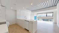 Located on Euclid Avenue in Cleveland's University Circle neighborhood, this single-floor unit showcases a clean, modern design characterized by crisp white walls, light wood-tone flooring, and an open, airy layout throughout.

The open-plan living area is generously proportioned, benefiting from large windows that invite abundant natural light and offer views of the surrounding urban landscape. Exposed metal ceiling details add an industrial edge, complementing the otherwise minimalist aesthetic.

The space features two distinct kitchen configurations. The primary kitchen presents a sleek, handleless design with a continuous white countertop, integrated sink with a pull-down faucet, and a dishwasher, all beneath a striking skylight that floods the area with daylight. A secondary galley-style kitchen is outfitted with white cabinetry, a ceramic cooktop range, over-the-range microwave, and a full-size refrigerator — offering practical, well-organized functionality.

The bathroom is finished in a cohesive white palette, featuring small-format mosaic floor tile, matching wall tile surrounding a full soaking tub with shower, and a vanity with sink. The space is simple, clean, and efficiently designed.

Throughout the unit, recessed lighting, roller shades, and thoughtfully placed outlets reflect careful attention to modern livability and comfort.
