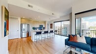 Located at 200 Nerem St NW in Atlanta, GA, this modern 2-bedroom, 2-bathroom residence offers a thoughtfully designed open-concept layout with contemporary finishes throughout. The combined kitchen and living area serves as the heart of the home, featuring light hardwood-style flooring, recessed lighting, and a striking oversized island with a white quartz countertop and seating for multiple guests. The kitchen is equipped with stainless steel appliances, light wood cabinetry, and a vibrant blue tile backsplash that adds a bold design accent. The living room is bathed in natural light through expansive floor-to-ceiling windows, which frame sweeping views of the Atlanta skyline and surrounding green spaces. Both bedrooms offer plush carpeting, large windows with city and landscape views, and dedicated closet space. The primary bathroom features a dual-sink vanity with light wood cabinetry and quartz countertops, alongside a walk-in closet. The secondary bathroom includes a full tub-shower combination with tile surround and a clean, minimalist vanity. A connecting hallway provides seamless flow between all spaces. The overall ambiance is bright, airy, and refined, reflecting a sleek urban aesthetic.