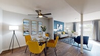 This well-appointed two-floor residence combines modern design with comfortable living across a thoughtfully laid-out floor plan. The open-concept main living area seamlessly connects the dining and living spaces, both finished with rich wood-look flooring. The dining area is anchored by a ceiling fan and features bold abstract wall art in blue and gold tones, complemented by striking mustard yellow chairs around a glass-top table. The adjacent living room continues the vibrant color palette with a deep teal accent wall, a neutral sofa accented with gold throw pillows, and a patterned area rug that ties the space together. Natural light filters in through window treatments throughout. The kitchen is equipped with stainless steel appliances, including a refrigerator and dishwasher, white shaker-style cabinetry, granite-look countertops, and a subway tile backsplash. A window above the sink brings in additional natural light. The bedroom offers plush carpeting, generous closet space, and a dramatic teal accent wall with large-scale artwork, creating a serene yet bold retreat. The bathroom features a white vanity with granite countertops, a framed mirror, and wood-look flooring, maintaining the cohesive design aesthetic found throughout the home.