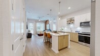 Located in Longwood, FL, this thoughtfully designed 2-bedroom, 2-bathroom residence offers a well-appointed single-floor layout that balances modern aesthetics with everyday functionality. The open-concept living, dining, and kitchen area serves as the heart of the home, highlighted by light wood-style flooring throughout and abundant natural light from multiple windows. The kitchen is a standout feature, showcasing two-tone cabinetry — crisp white uppers paired with warm natural wood lowers — white subway tile backsplash, quartz countertops, stainless steel appliances, open shelving, and a central island with bar seating illuminated by pendant lighting. The living room features a distinctive arched accent wall in warm terracotta tones, a ceiling fan, and direct access to a private balcony overlooking a lushly landscaped courtyard with a pool area and palm trees. The generously sized primary bedroom includes large windows, a ceiling fan, a walk-in closet with built-in shelving, and an en-suite bathroom with a glass-enclosed walk-in shower with white tile surround. The second bedroom is equally well-lit with outdoor views. Three closets, a dedicated laundry area, and two full bathrooms complete the layout, offering ample storage and comfort throughout.