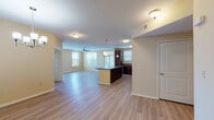 This single-floor residence offers a well-designed open-concept layout that seamlessly connects the living, dining, and kitchen areas. Light wood-look flooring runs throughout the main living spaces, complemented by neutral warm-toned walls that create a bright and welcoming atmosphere. A ceiling fan in the living area and multiple windows allow natural light to filter in, enhancing the sense of spaciousness.

The kitchen is a standout feature, equipped with rich dark-wood cabinetry, dark granite-style countertops, and a full suite of black appliances including a refrigerator, range, built-in microwave, and dishwasher. A central island with additional counter space adds both functionality and a natural division between the kitchen and living areas. Pendant lighting above the island adds a polished touch.

A carpeted hallway leads to the private areas of the unit, including a walk-in closet fitted with wire shelving and dual hanging rods for ample storage. Two bathrooms are present: one featuring a tiled walk-in shower with grab bars, and the other offering a tiled tub-shower combination, each with dark wood vanities and hard-surface countertops.

The dedicated laundry room accommodates a full-size washer and dryer with an overhead drying rack, adding everyday convenience to this thoughtfully arranged space.