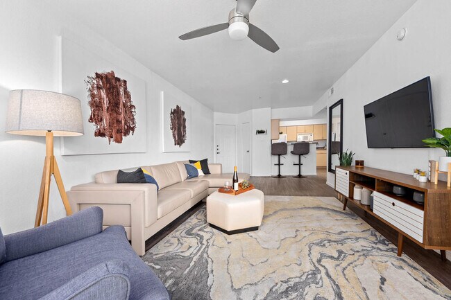 Living room with beige sectional, ceiling fan and wall-mounted TV on hardwood floors - Monterra