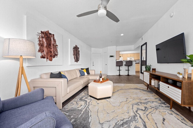 Living room with beige sectional, ceiling fan and wall-mounted TV on hardwood floors - Monterra