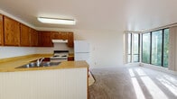 Located at 5215 Mockingbird Drive in Anchorage, Alaska, Unit 206 is a single-floor residence offering a well-organized and functional layout. The open-concept living and kitchen area is a central feature, flooded with natural light through large floor-to-ceiling corner windows that frame views of the surrounding Alaskan greenery. Plush wall-to-wall carpeting extends throughout the living space, adding warmth underfoot.

The kitchen is equipped with rich wood cabinetry, a butcher-block-style countertop, a stainless steel double sink, a white electric range, and a full-size refrigerator. A beadboard-paneled peninsula provides a natural divide between the kitchen and the carpeted living area, which also features a ceiling fan overhead.

The bedroom is a comfortable, well-lit room with a large window overlooking outdoor greenery and includes a dedicated closet with sliding panel doors and built-in shelving. A hallway connects the rooms efficiently, featuring dark wood door frames and trim throughout that provide a classic contrast against the light-toned walls and ceilings.

The bathroom includes tile flooring, a wooden vanity with countertop, a bathtub, and ample functional space. A textured ceiling in the hallway area adds a subtle design detail. Overall, the unit offers a practical and comfortable living environment in a natural Alaskan setting.