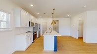 Located at 1748 Marglyn Drive in Matthews, NC, this well-appointed two-story home offers four bedrooms and five bathrooms across two thoughtfully designed floors. The main level opens into a bright, open-concept living, dining, and kitchen area finished with warm light hardwood flooring throughout. The kitchen is a standout, featuring crisp white shaker cabinetry with gold hardware, stainless steel appliances, and a striking center island with a bold cobalt blue base, white countertop, and brushed gold pendant lighting overhead. A sleek pedestal-sink powder room and a pantry round out the main floor, alongside a spacious attached garage with an automatic opener. The upper level hosts all four bedrooms, each filled with natural light from well-positioned windows. The primary bedroom is generously sized, accompanied by a walk-in closet with wire shelving that maximizes storage. Additional bedrooms feature double-door closets and the same consistent hardwood-style flooring. A conveniently located upper-level laundry room is equipped with a full-size washer and dryer. With seven closets total, three hallways, and five bathrooms distributed across both floors, this home delivers practical functionality alongside clean, modern finishes throughout.