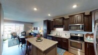 The Sonoma model unit in Maple Grove, Minnesota, offers a thoughtfully designed one-bedroom, one-bathroom single-floor layout that balances comfort and modern style. The open-concept living and kitchen area is anchored by a chef-inspired kitchen featuring rich dark-stained cabinetry, granite countertops, a subway tile backsplash, stainless steel appliances, and a large center island with bar seating — ideal for both meal preparation and casual dining. Hardwood-style flooring flows throughout the main living areas, complementing the warm, neutral color palette. The living room is generously proportioned, bathed in natural light from large sliding glass doors that open onto a private balcony with outdoor views. The bedroom is a calm retreat, appointed with plush carpeting, a ceiling fan, and ample natural light from a window overlooking the surrounding community. The full bathroom features granite countertops, dark wood cabinetry with a framed mirror, and a tub-shower combination with tile surround. Recessed lighting throughout the unit enhances the bright, welcoming ambiance. The Sonoma presents a well-rounded living space suited for those seeking contemporary design and functional comfort in Maple Grove.