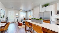 This single-story unit offers a thoughtfully organized layout across a compact yet efficient floor plan. The open-concept kitchen and living area serves as the heart of the space, where clean sightlines connect both functional zones seamlessly. The kitchen is outfitted with white shaker cabinetry, white quartz countertops, stainless steel appliances including a refrigerator, range, microwave, and dishwasher, and a peninsula island with bar seating for two. Natural light streams through multiple windows fitted with horizontal blinds and sheer curtains. The living area accommodates comfortable seating and media storage, with a ceiling fan overhead and direct access to an entry door. Hardwood-style flooring extends consistently throughout the unit, contributing to a cohesive aesthetic. The bedroom features a ceiling fan, a window with outdoor views, soft neutral wall tones, and direct access to a dedicated walk-in closet equipped with built-in shelving. The bathroom includes a white vanity with quartz countertop, a sliding-door shower enclosure, and matching white cabinetry. A hallway connects the private areas to the main living space, completing the efficient and modern layout.