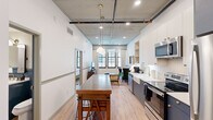 Located at 808 Constance St in New Orleans' vibrant Lower Garden District, this thoughtfully designed 2-bedroom, 1-bathroom unit blends industrial character with contemporary comfort. Exposed concrete ceilings with visible ductwork and structural pipes give the space a loft-like aesthetic, while light hardwood flooring and crisp white walls keep the atmosphere bright and modern.

The open-concept kitchen anchors the main living area and is outfitted with two-tone cabinetry — slate blue lower cabinets paired with white uppers, brass hardware, a farmhouse sink, white subway tile backsplash, and a full suite of stainless steel appliances. A freestanding wooden island with bar seating adds both function and warmth. The living area beyond receives generous natural light through large industrial-style windows.

The primary bedroom is a serene retreat featuring exposed concrete ceilings, large black-framed windows overlooking the neighboring brick facade, light hardwood floors, and a ceiling fan. A second bedroom offers similar finishes and a wall-mounted TV. The shared bathroom is elegantly appointed with a navy vanity, brass fixtures, a large mirror, and a glass-enclosed walk-in shower with patterned tile. Every detail reflects a cohesive, urban design sensibility ideal for New Orleans living.