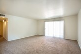 This single-story residence offers a practical and straightforward layout designed for comfortable everyday living. The spacious living area is finished with neutral wall-to-wall carpeting and features a large sliding glass door fitted with vertical blinds, allowing natural light to filter in while providing access to an outdoor area. The open feel of the room is reinforced by clean white walls and a smooth ceiling.

The galley-style kitchen is efficiently organized with warm wood-toned cabinetry lining both walls, offering generous storage above and below the white countertops. White appliances, including a refrigerator, electric range, and dishwasher, are integrated into the layout, and durable wood-look flooring runs the length of the kitchen for easy maintenance.

The bedrooms are carpeted and bright, each featuring windows with blinds that bring in natural light. The primary bedroom is notably well-equipped with dual closets providing ample storage. An additional bedroom includes a built-in shelf and a window with an exterior view.

The full bathroom features a tub-shower combination, a single-sink vanity with white cabinetry, a large mirror, and wood-look flooring that complements the kitchen. The overall aesthetic throughout the space is clean and neutral, offering a functional and move-in ready environment.