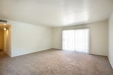 This single-story residence offers a practical and straightforward layout designed for comfortable everyday living. The spacious living area is finished with neutral wall-to-wall carpeting and features a large sliding glass door fitted with vertical blinds, allowing natural light to filter in while providing access to an outdoor area. The open feel of the room is reinforced by clean white walls and a smooth ceiling.

The galley-style kitchen is efficiently organized with warm wood-toned cabinetry lining both walls, offering generous storage above and below the white countertops. White appliances, including a refrigerator, electric range, and dishwasher, are integrated into the layout, and durable wood-look flooring runs the length of the kitchen for easy maintenance.

The bedrooms are carpeted and bright, each featuring windows with blinds that bring in natural light. The primary bedroom is notably well-equipped with dual closets providing ample storage. An additional bedroom includes a built-in shelf and a window with an exterior view.

The full bathroom features a tub-shower combination, a single-sink vanity with white cabinetry, a large mirror, and wood-look flooring that complements the kitchen. The overall aesthetic throughout the space is clean and neutral, offering a functional and move-in ready environment.