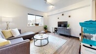 Located at 478 E Beaver Ave in the heart of State College, PA, this one-bedroom, one-bathroom unit offers a thoughtfully designed layout across a single floor. The space makes efficient use of every square foot, presenting a clean, modern aesthetic throughout.

The living room serves as the central gathering space, featuring warm wood-look flooring, track lighting on a paneled ceiling, and a large window that fills the room with natural light and frames views of the surrounding cityscape. The open feel of the room is enhanced by crisp white walls and a well-proportioned layout.

The bedroom is a well-defined private retreat, equipped with a platform bed featuring under-bed storage drawers, a bold dark wardrobe unit with mesh paneling, and an additional open clothing rack — maximizing storage in a smart, contemporary way. Track lighting continues here, maintaining a consistent design language throughout the unit.

The bathroom is clean and modern, showcasing a gray shaker-style vanity with white quartz countertops, an undermount sink, and a large mirror. Wood-look flooring carries through from the main living areas, tying the space together cohesively.

Overall, this unit delivers a modern urban living experience with functional design details, consistent finishes, and a bright, airy ambiance well-suited for life in downtown State College.