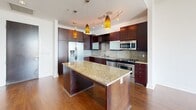 Located at 1400 Hi Line Dr in Dallas's vibrant Design District, this one-bedroom, one-bathroom residence offers a thoughtfully designed single-floor layout with contemporary finishes throughout. Rich hardwood flooring flows seamlessly across the living areas, complementing the clean, modern aesthetic of the space.

The kitchen is a standout feature, showcasing dark espresso cabinetry that reaches toward the ceiling, a textured stone-tile backsplash, and gleaming granite countertops. A central island provides additional prep space and casual seating, while stainless steel appliances — including a refrigerator, gas range, and built-in microwave — add a polished, professional feel. Distinctive amber pendant lights overhead complete the warm yet sophisticated atmosphere.

The bedroom is a bright, comfortable retreat featuring rich hardwood floors, a ceiling fan, and a large picture window that frames sweeping views of the Dallas skyline and surrounding cityscape, flooding the room with natural light.

The bathroom is finished with large-format dark tile surrounding a soaking tub and shower, paired with a granite-topped vanity and dark wood cabinetry, creating a spa-like ambiance. A hallway with recessed lighting connects the rooms, keeping the layout efficient and flowing. This residence combines urban style with functional living in one of Dallas's most dynamic neighborhoods.