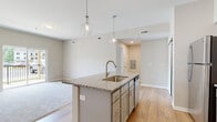 Located at 311 W Johnstown Rd in Gahanna, Ohio, this modern single-floor residence offers a well-designed open-concept layout that seamlessly connects the kitchen, dining, and living areas. The kitchen serves as the centerpiece of the space, showcasing a large granite-topped island with an undermount sink and pendant lighting overhead. Gray shaker-style cabinetry lines the walls, complemented by a classic subway tile backsplash and a full suite of stainless steel appliances, including a refrigerator, range, and microwave. Light-toned hardwood flooring flows throughout the main living areas, adding warmth and continuity to the design. The living area is finished with plush carpeting and features sliding glass doors that open onto a private balcony with outdoor views, allowing for excellent natural light. A dedicated in-unit laundry area with a stacked washer and dryer adds everyday convenience. The bathroom is thoughtfully appointed with a gray vanity, lit mirror, and light hardwood-style flooring. The bedroom is carpeted and features a large window that brings in natural light. Throughout the space, neutral tones, clean lines, and modern finishes create a cohesive and contemporary atmosphere.
