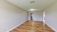 Located at 6860 Prutzman Rd in Beaumont, TX, this single-story 2-bedroom, 1-bathroom home offers a clean, updated interior with a consistent design aesthetic throughout. Wood-look luxury vinyl plank flooring runs through every room, complemented by light gray walls, crisp white baseboards, and textured ceilings that lend a classic residential character to the space.

The living room is an open, welcoming area filled with natural light from a front-facing window, anchored by a flush-mount ceiling fixture and direct access to the kitchen. The galley-style kitchen is well-appointed with gray shaker cabinets, white countertops, stainless steel appliances including a refrigerator and range, and notably includes an in-unit washer and dryer — a convenient and practical feature.

Both bedrooms are comfortably sized, each featuring ceiling fans with light kits and windows that bring in natural light. The spacious primary bedroom offers ample room for full bedroom furniture arrangements. The full bathroom includes a gray vanity with white countertop, an overhead medicine cabinet, and a full tub-shower combination with white surround. Two closets and a hallway provide additional storage throughout the home.